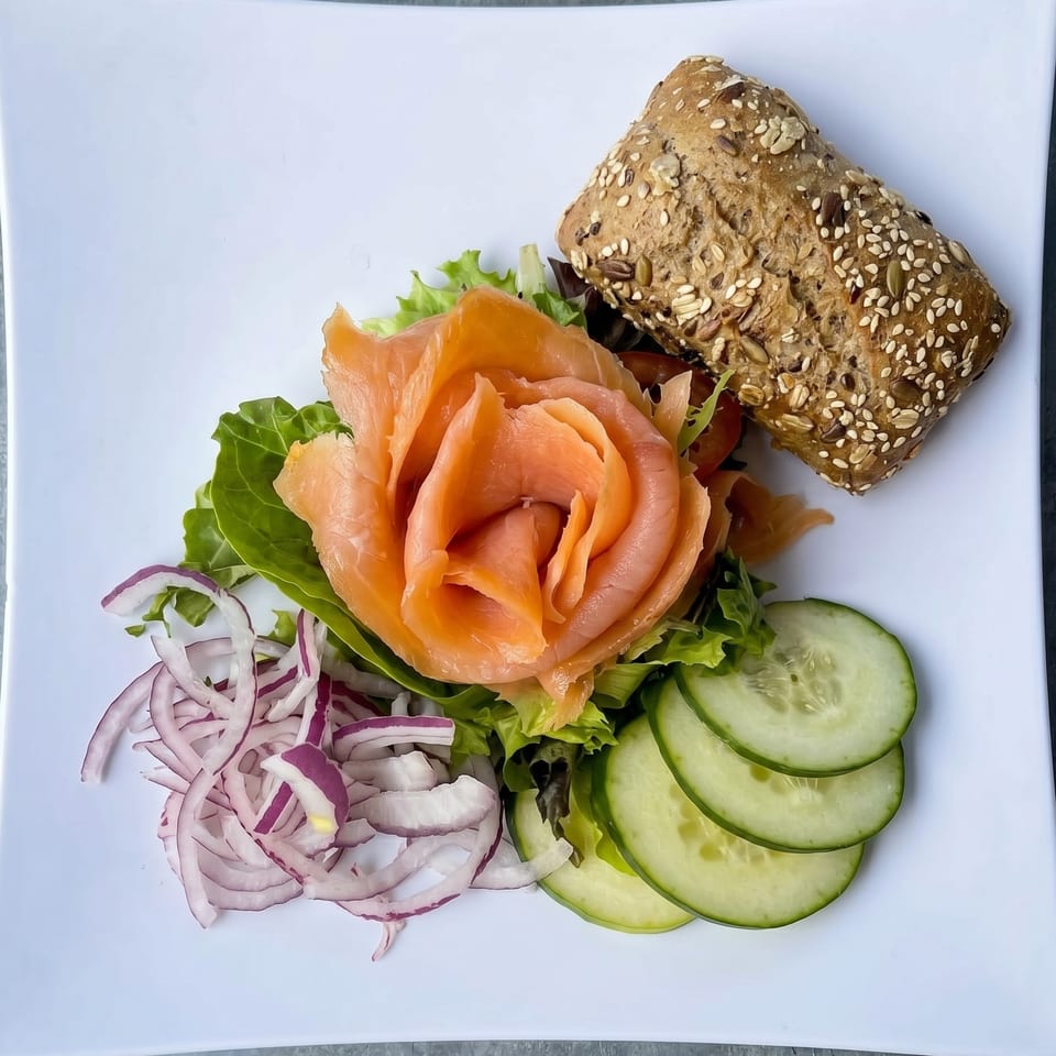 Smoked salmon arranged like a rose, with lettuce, red onions, cucumber, and a seeded bread roll.